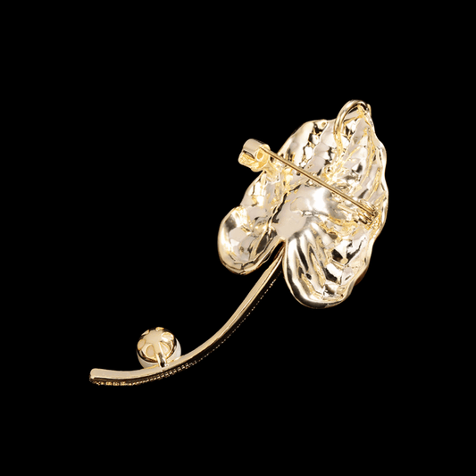 AVELIA textured gold calla lily brooch with purple crystal center and pearl accent on a curved stem.