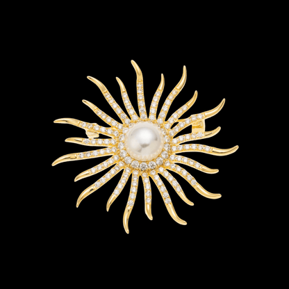 AVELIA gold sun brooch featuring a large central pearl surrounded by curved, crystal-lined rays on a black background.