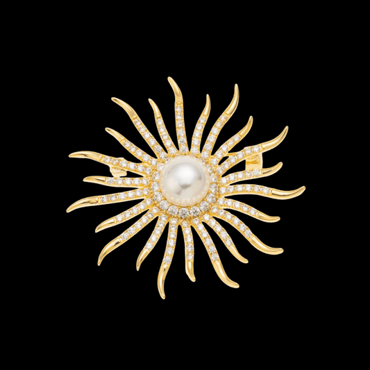 AVELIA gold sun brooch featuring a large central pearl surrounded by curved, crystal-lined rays on a black background.