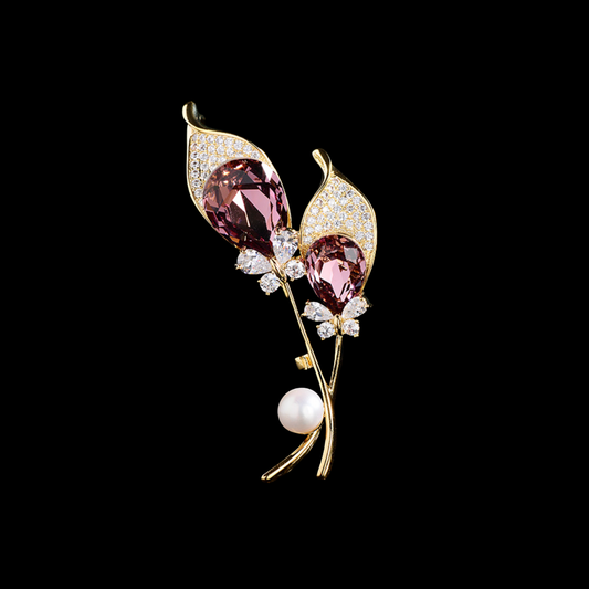 AVELIA gold double calla lily brooch featuring two large purple teardrop crystals, petal edges, and a white pearl accent on a black background.