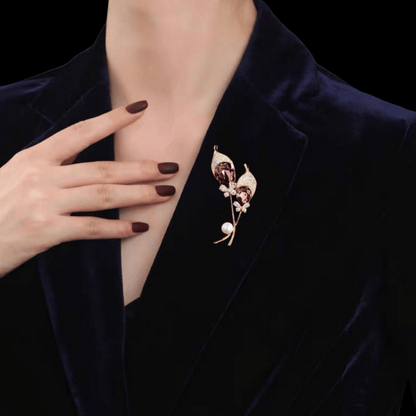 AVELIA gold double calla lily brooch featuring two large purple teardrop crystals, petal edges, and a white pearl accent on a black background.